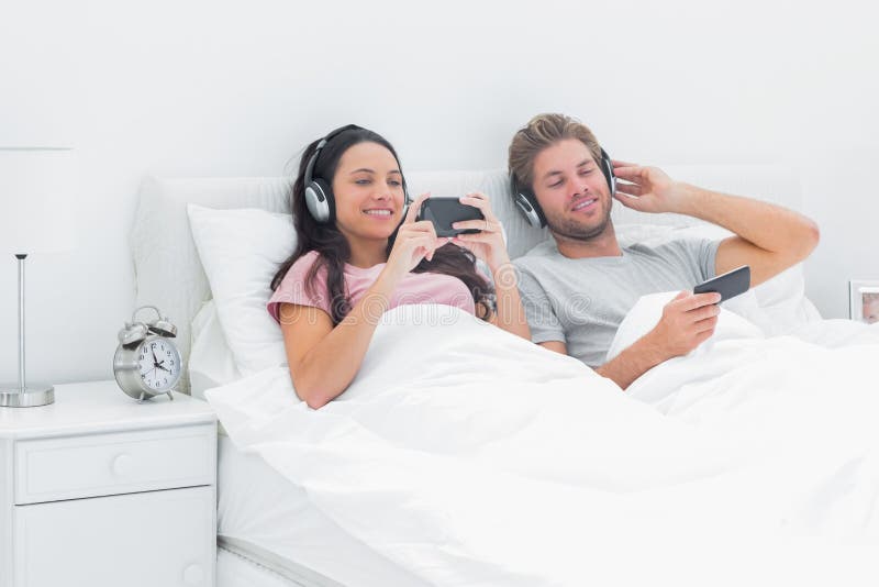 Beautiful couple listening to music in their bed with smartphones