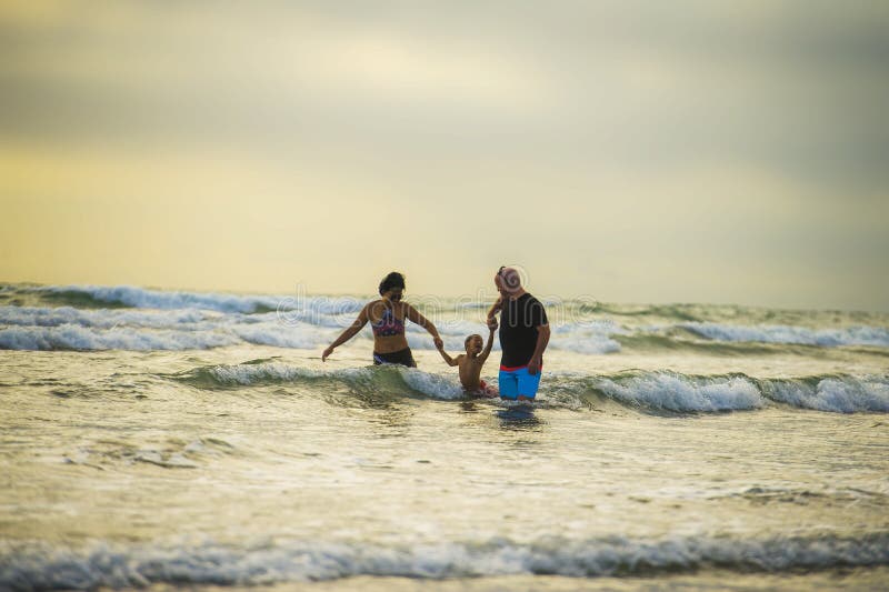 Couple and little son walking relaxed on sunset beach enjoying romantic Summer holidays family trip the parents holding the child