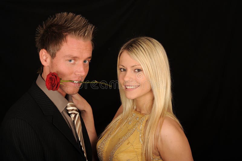 A formal studio portrait of a lovely young couple with a the man holding a long stem rose in his mouth. Black background. A formal studio portrait of a lovely young couple with a the man holding a long stem rose in his mouth. Black background.