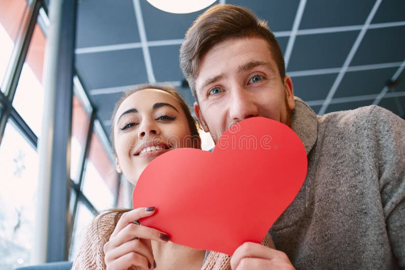 Couple in love on a date in cafe in Valentines day. Man and women smiling and holding a large paper heart. Two people, men and women in cafe communicate stock photo