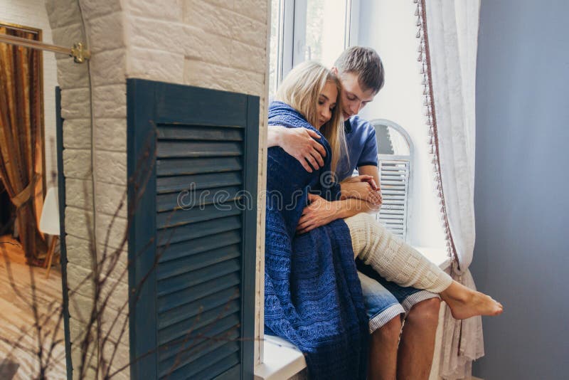 Couple in love sitting at home on the window. Tender loving embrace of newlyweds. Fun morning happy mood of a loving couple. Girl