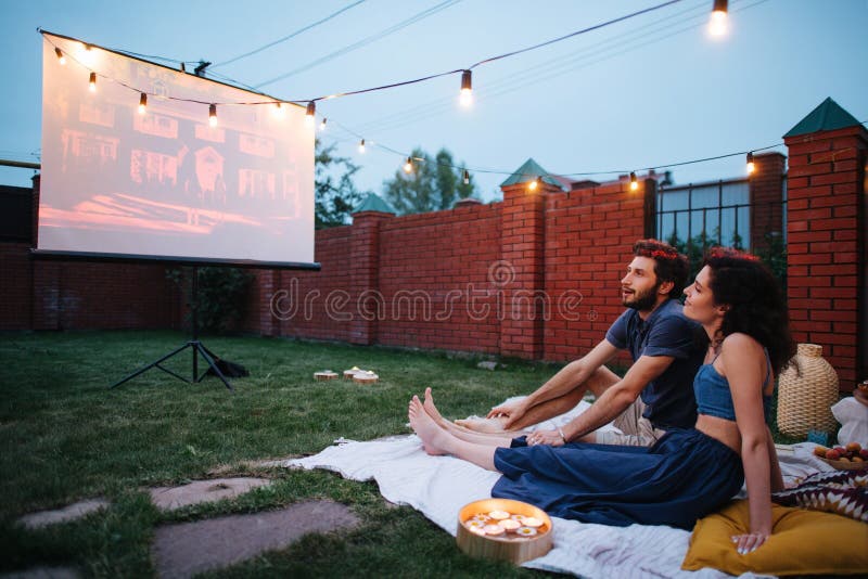 Couple in love watching a movie, in twilight, outside on the lawn in a courtyard