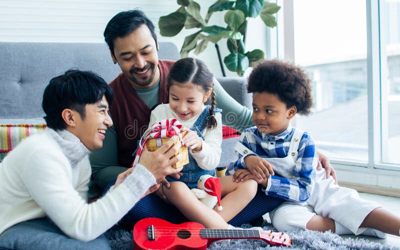 Couple male gay taking care, giving gift to adopted children who are little diverse Caucasian and African girl and boy with