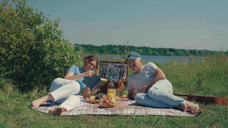 A couple, a man and a woman read a book in nature in the summer.