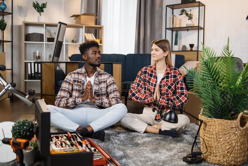 Couple meditating at new flat with boxes and tools around royalty free stock photos