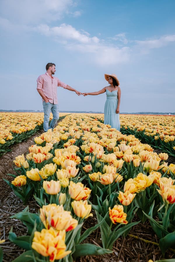 Couple men and woman in flower field in the Netherlands during Spring, orange red tulips field near Noordoostpolder Flevoland Netherlands, men and woman in Spring evening sun, flowers