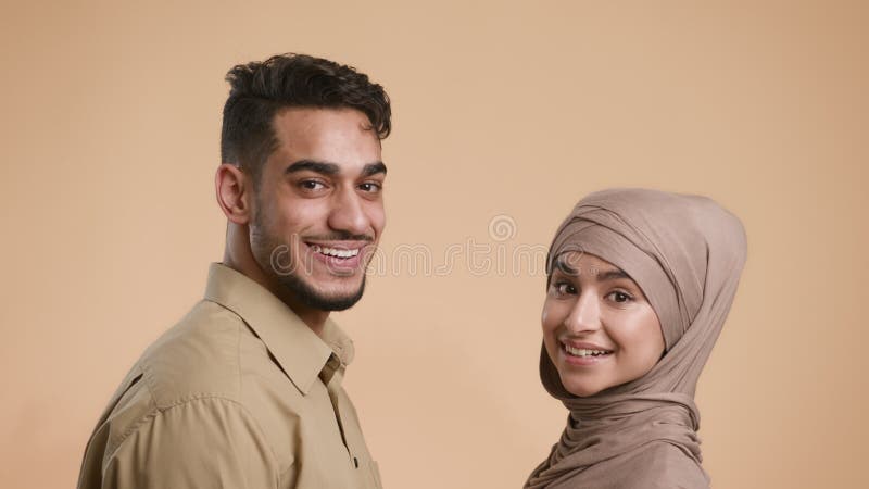Couple musulman tournant la tête et souriant debout sur fond beige clips vidéos