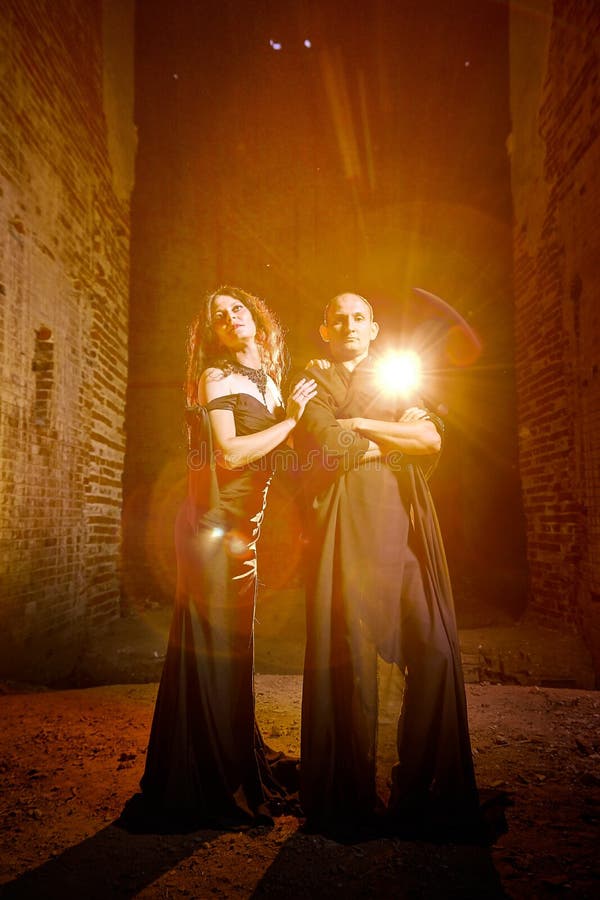 A couple in old dark clothes in an abandoned castle with old brick walls. A man and a woman posing in a dark gloomy