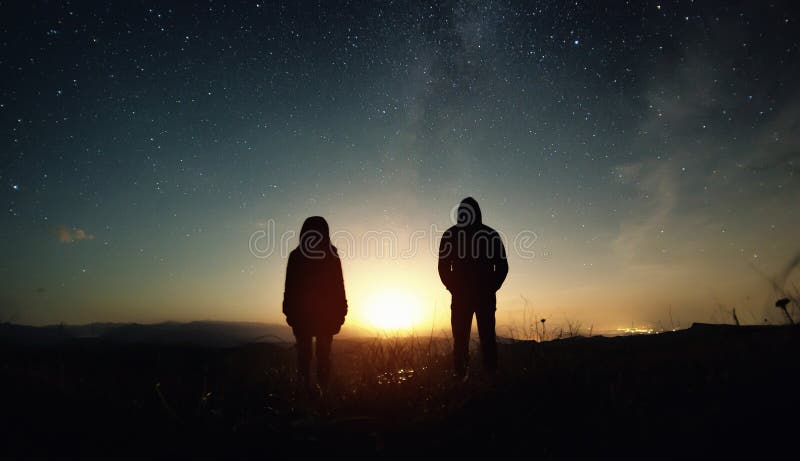 A couple of people man and woman stand at the sunset of the moon under the starry sky with bright stars and a milky way. Silhouettes of a guy and a girl standing royalty free stock photos