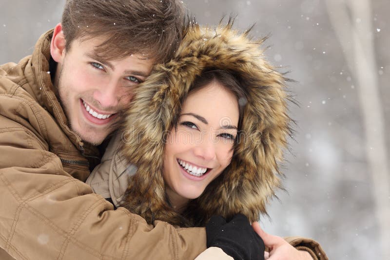 Couple smiling with perfect teeth hugging and looking at camera in winter in a forest. Couple smiling with perfect teeth hugging and looking at camera in winter in a forest