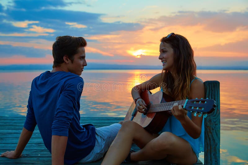 Couple playing guitar in sunset pier at dusk beach