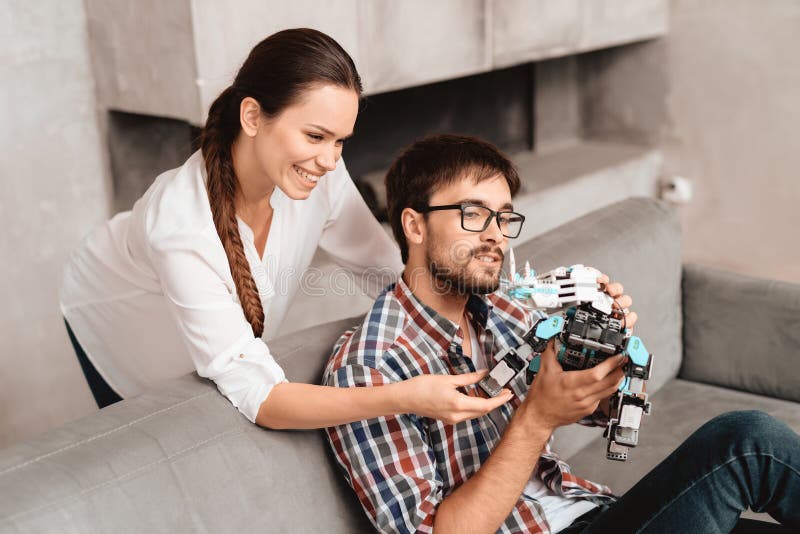 The couple plays with the robot a rhinoceros. The guy sits on the couch and holds the robot in his hands.