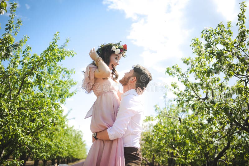 Couple portrait of a girl and guy looking for a wedding dress, a pink dress flying with a wreath of flowers on her head on a backg