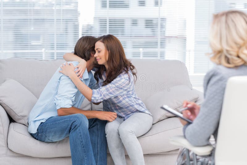 Couple reaching break through in therapy session sitting on the couch as therapist watches. Happy embracing couple stock images, royalty-free photos and pictures