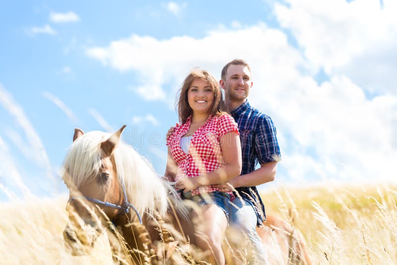 Couple riding on horse in meadow