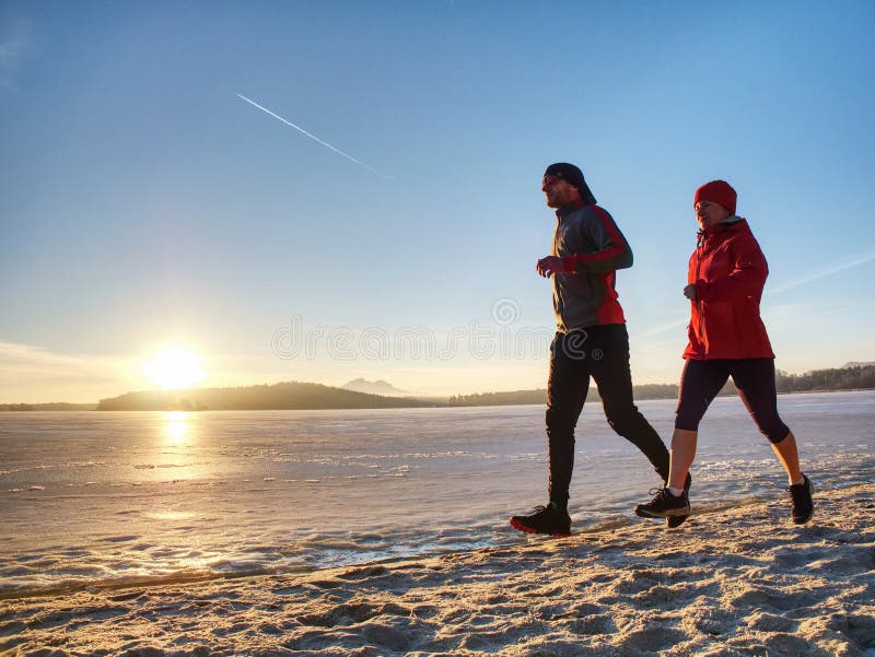 Couple runners running in winter nature. Frozen river