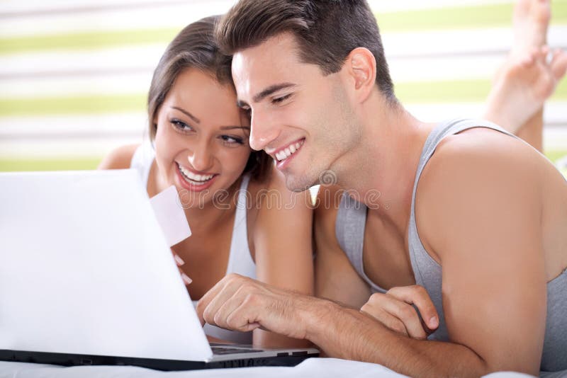 Happy young couple shopping online while lying on their bed. Happy young couple shopping online while lying on their bed