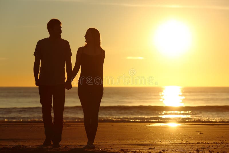 Couple silhouette walking together on the beach stock images