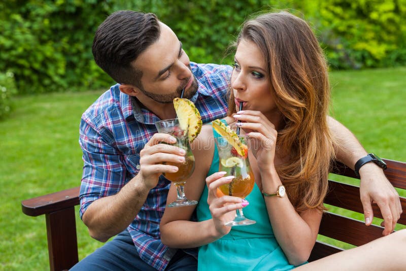 Couple sitting behind the table in garden and having colorful drinks