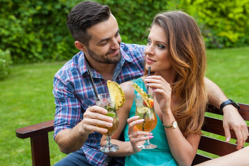 Couple sitting behind the table in garden and having colorful drinks