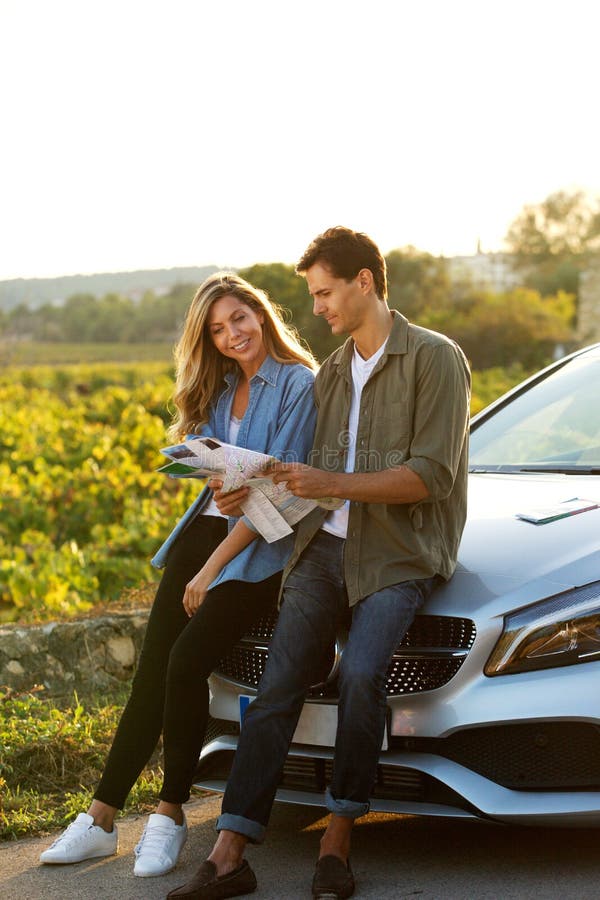 Couple sitting on hood of car looking at map.