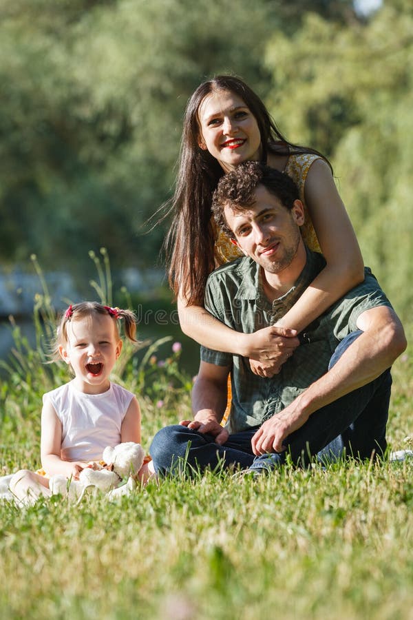 Couple sitting and hugging. Daughter is sitting next to and holding a Teddy bear. In the background the lake.