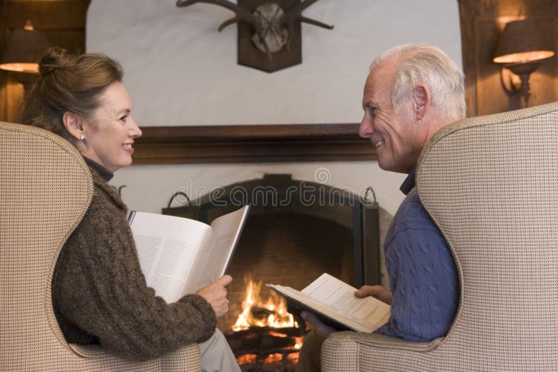 Couple sitting in living room by fireplace reading looking away from the camera
