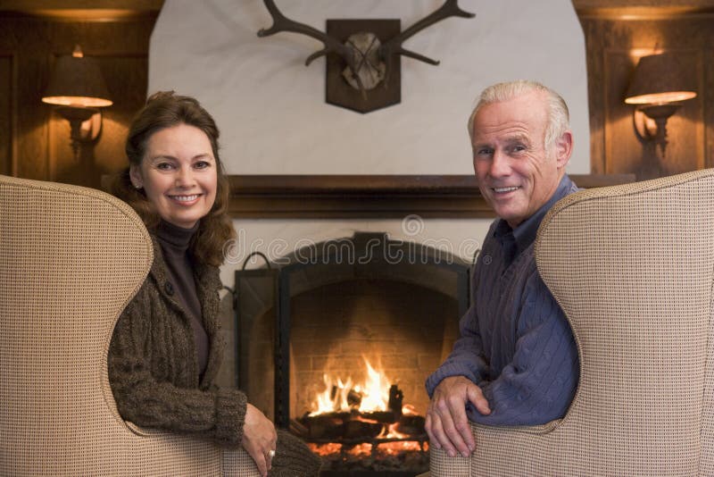 Couple sitting in the living room by fireplace smiling at camera. Couple sitting in the living room by fireplace smiling at camera