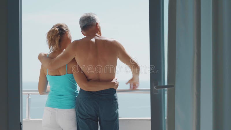 A slender elderly couple, a man and a woman, stand on the balcony, hugging each other and enjoying