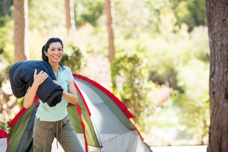 Rolled sleeping bag resting beside pitched dome tent in sunlit pine forest clearing, copy space stock photo