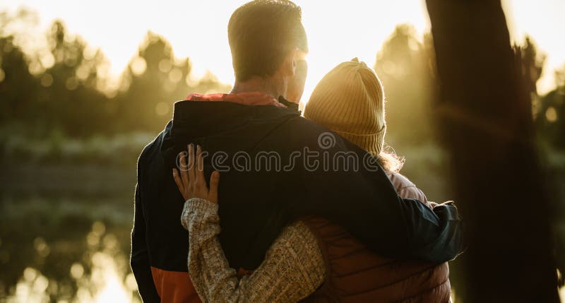 Rear view of couple standing together by the lake. Man and women in warm clothing looking at a view. Rear view of couple standing together by the lake. Man and women in warm clothing looking at a view