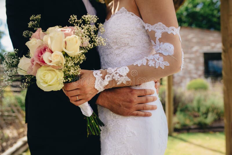 Mid section of couple standing together on their wedding day. Bride and groom with a flower bouquet.