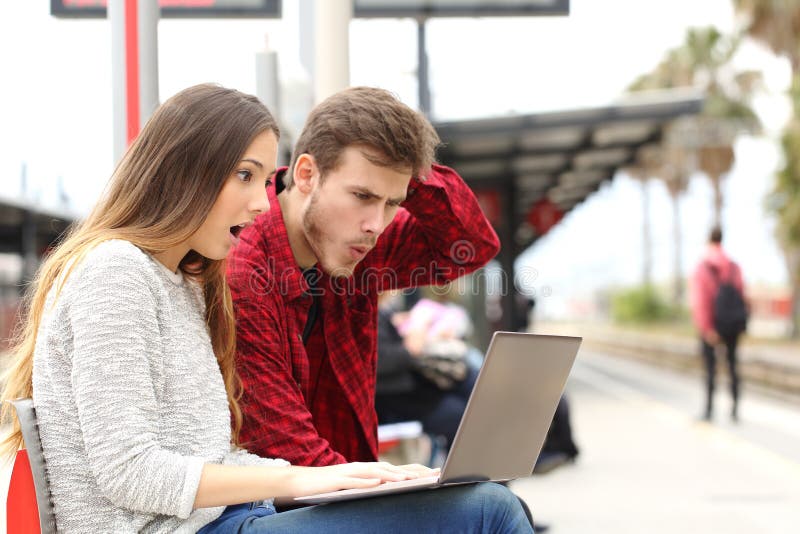 Couple worried and surprised watching a laptop in a train station while they are waiting. Couple worried and surprised watching a laptop in a train station while they are waiting