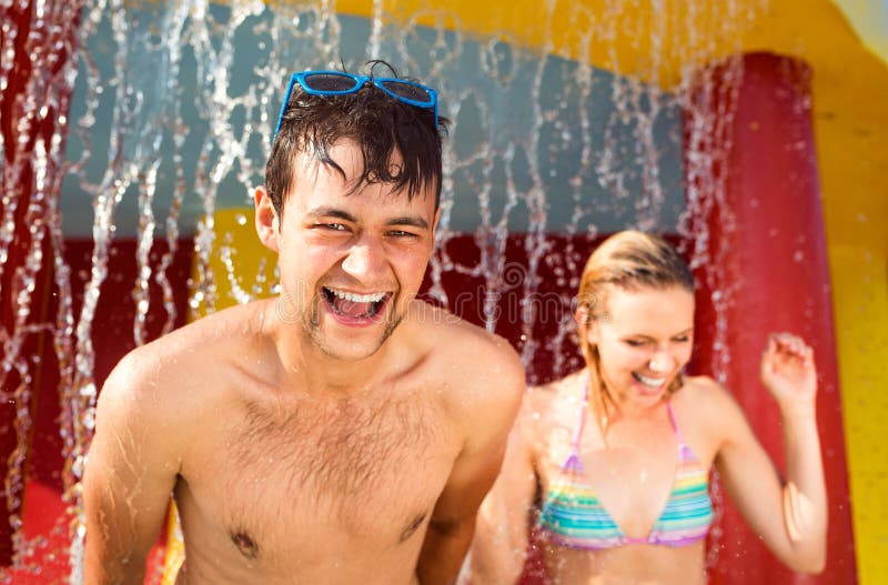 Couple in swimmning suits under splashing fountain. Summer heat.