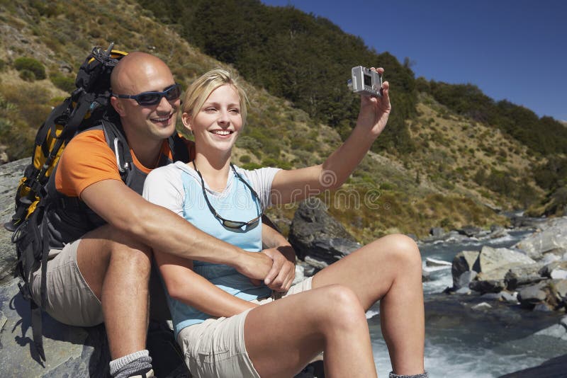 Man hugging women as she takes their picture by river in the forest. Man hugging women as she takes their picture by river in the forest