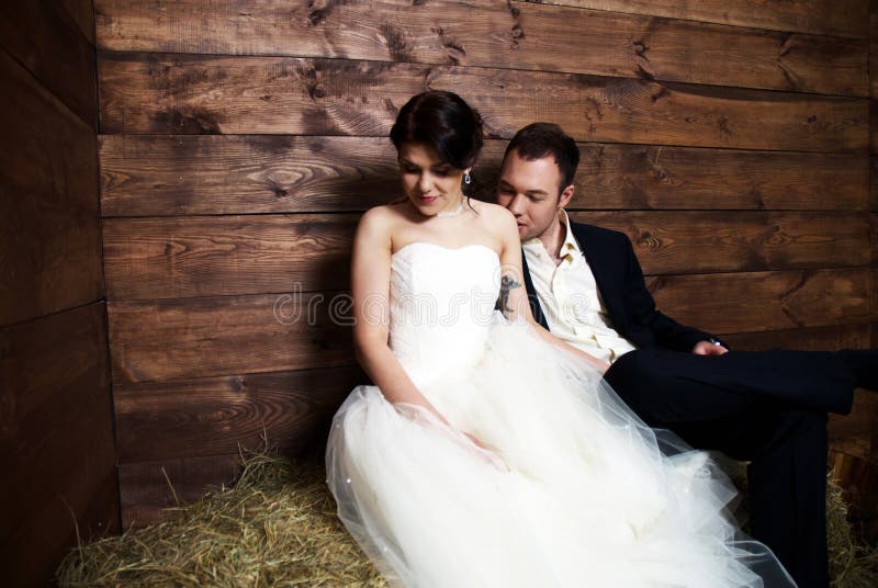 Couple in their wedding clothes in barn with hay