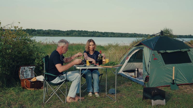 A couple of tourists, a man and a woman are resting with a tent by the river.