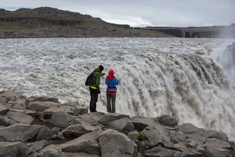 A couple of tourists stand on the very edge of the powerful waterfall Dettifos stock images A couple of tourists stand on the very edge of the powerful waterfall Dettifos stock images