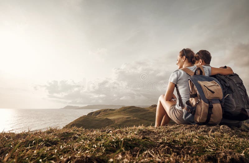 Couple travelers with backpacks look sunset on top of a mountain