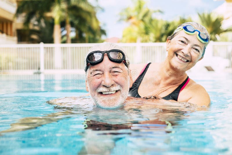 Couple of two seniors hugged in the water of swimming pool - active man and woman doing exercise together at the pool - hugged