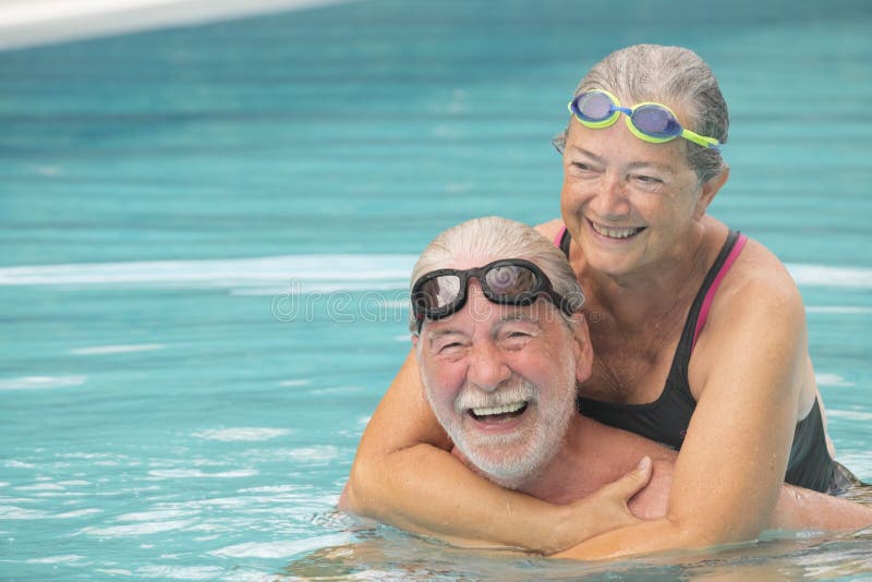 Couple of two seniors hugged in the water of swimming pool - active man and woman doing exercise together at the pool - hugged