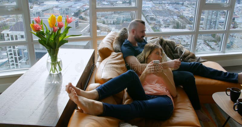 Couple using digital tablet and mobile phone in living room 4k