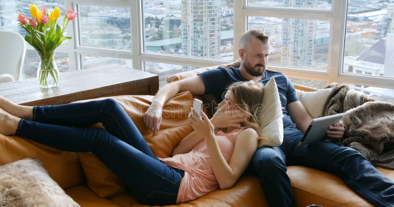 Couple using digital tablet and mobile phone in living room 4k