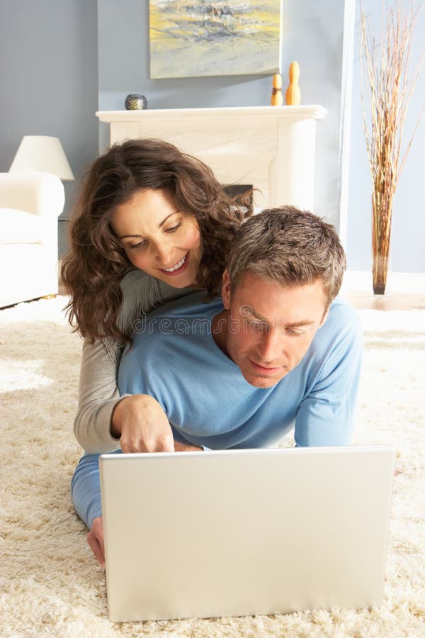 Couple Using Laptop Relaxing Laying On Rug At Home