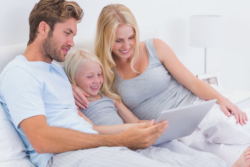 Couple using a laptop with their daughter in bed
