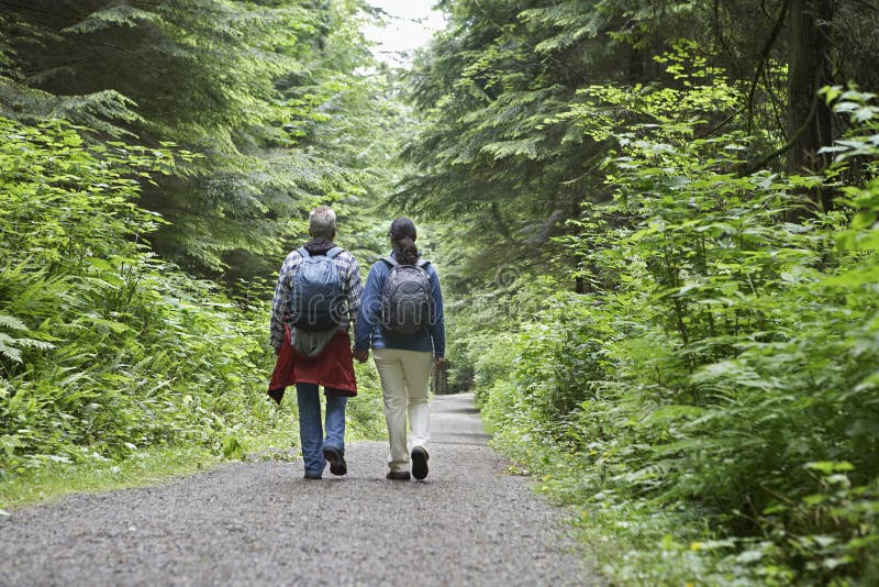 Couple Walking On Forest Road. Full length rear view of a couple walking on forest road amid lush trees stock photos Couple Walking On Forest Road. Full length rear view of a couple walking on forest road amid lush trees stock photos
