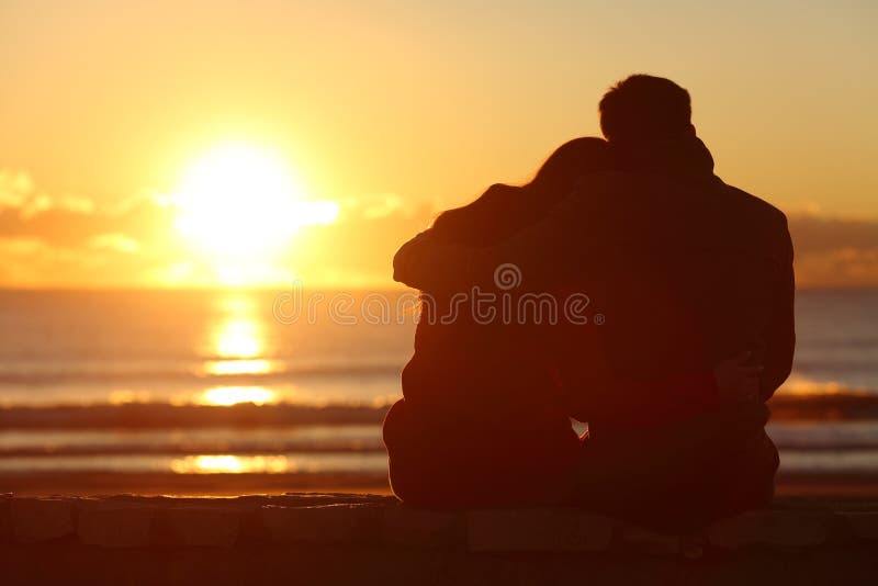 Back view of a couple silhouette watching sun at sunset on the beach in winter with a warmth light. Back view of a couple silhouette watching sun at sunset on the beach in winter with a warmth light