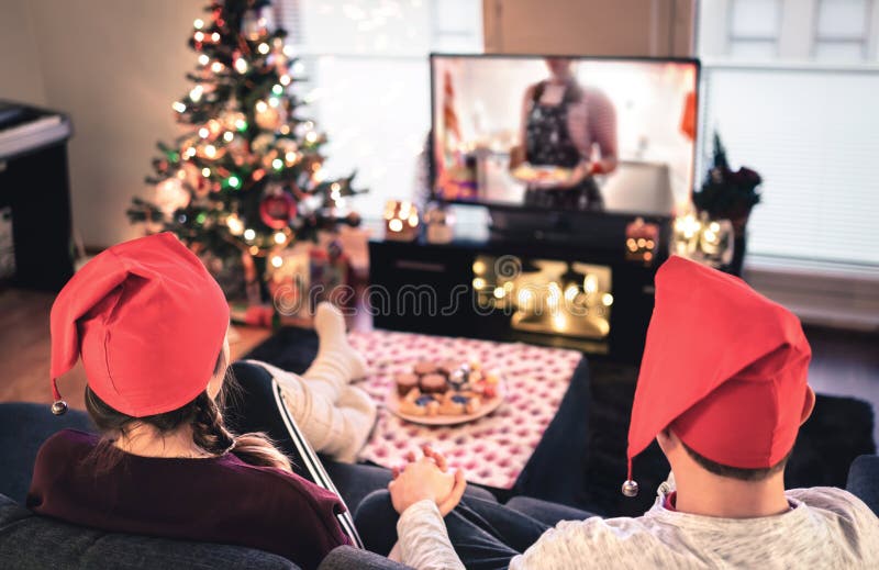 Couple watching tv on Christmas. Happy family holiday at home. Man and woman on couch relaxing with tree, decorations, lights.