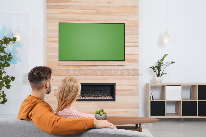 Couple watching TV on sofa in living room with decorative fireplace. Couple watching TV on sofa in living room with decorative fireplace