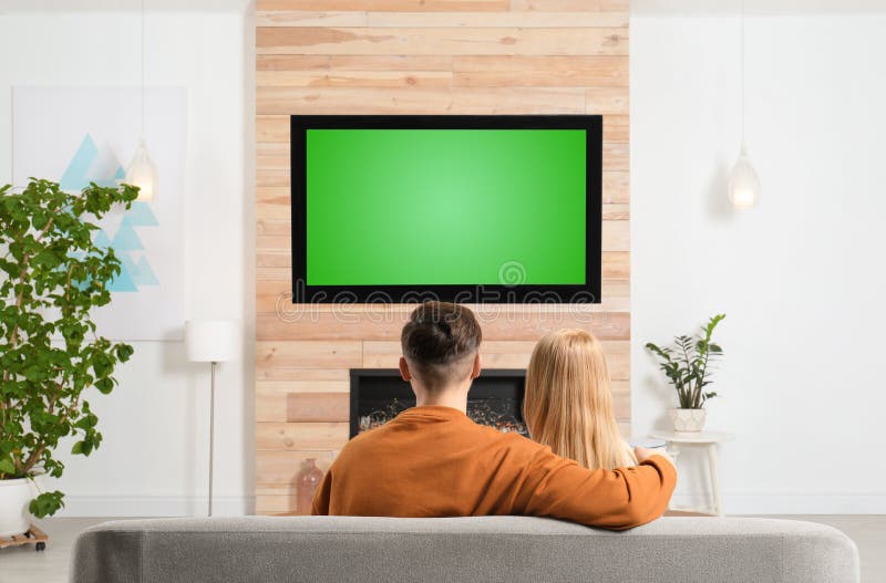 Couple watching TV on sofa in living room with decorative fireplace. Couple watching TV on sofa in living room with decorative fireplace